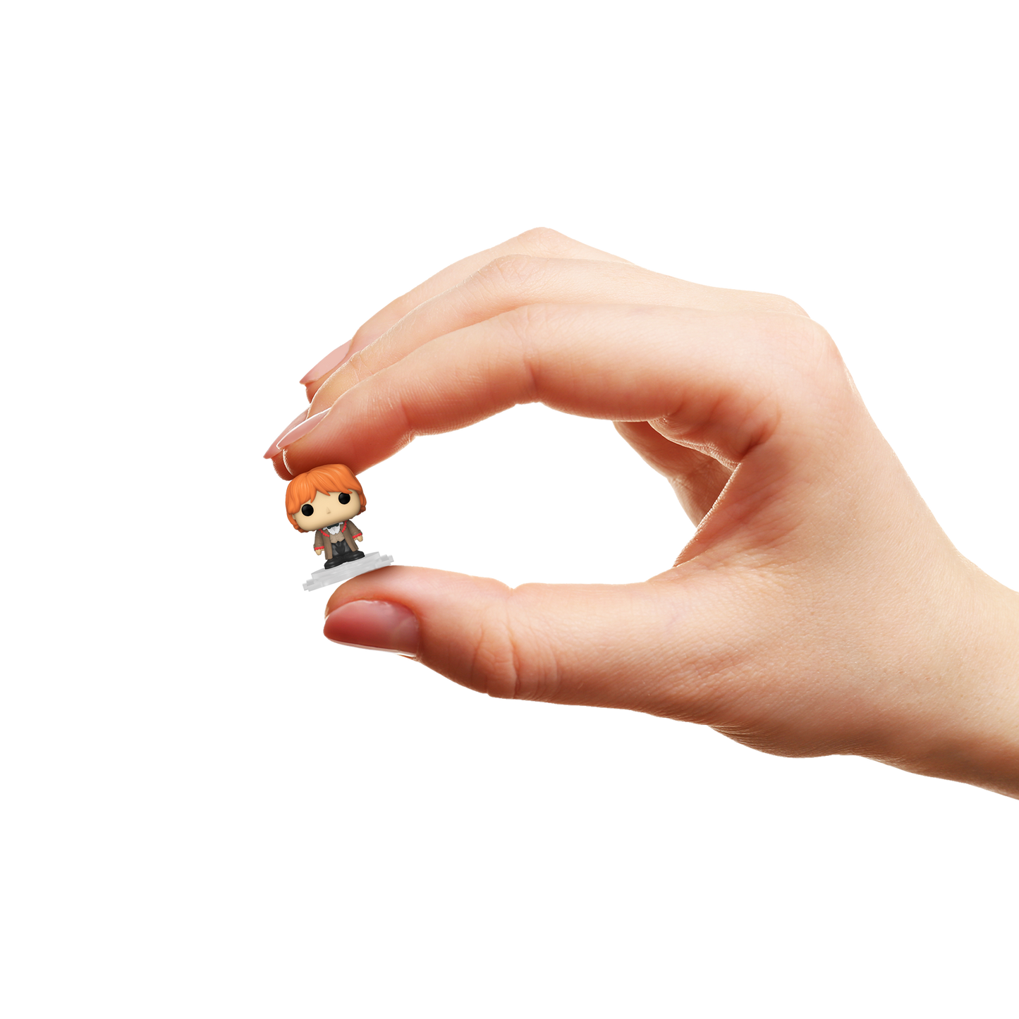 Hand holding a small figurine of Ron Weasley against a white background
