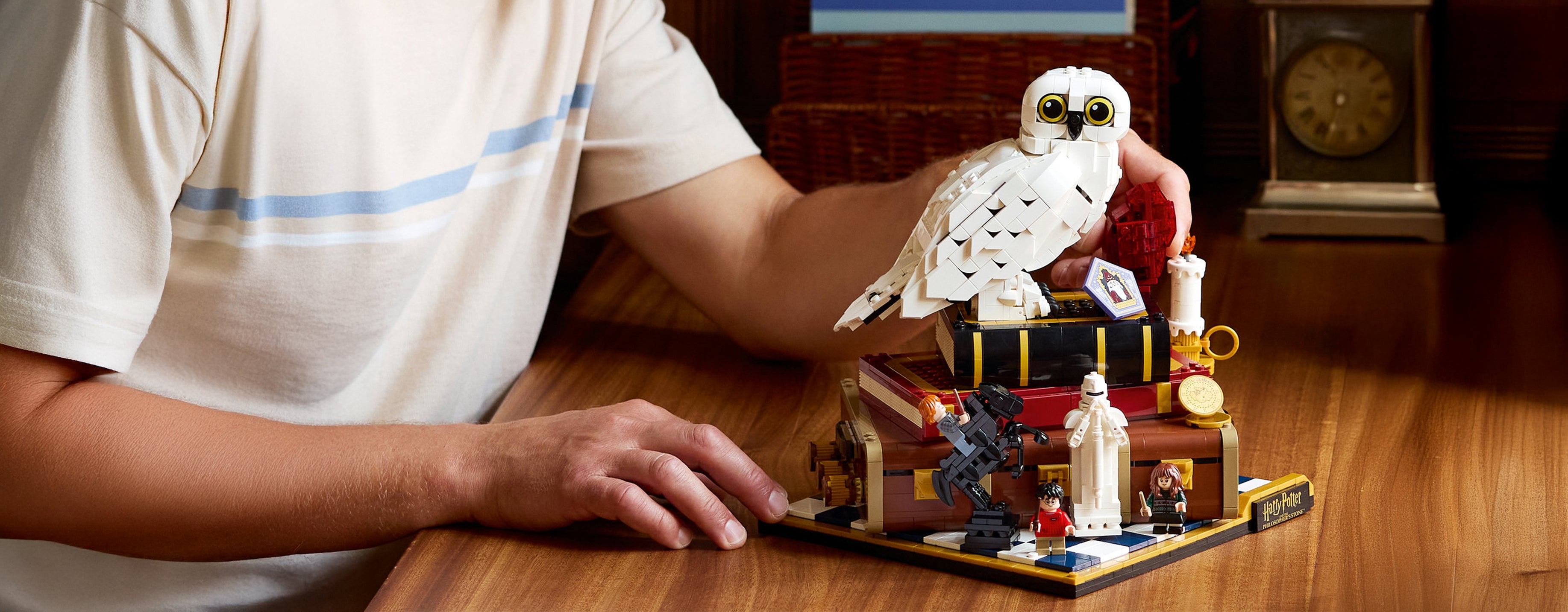 Person assembling a detailed LEGO set of Hedwig and chess set on a wooden table.