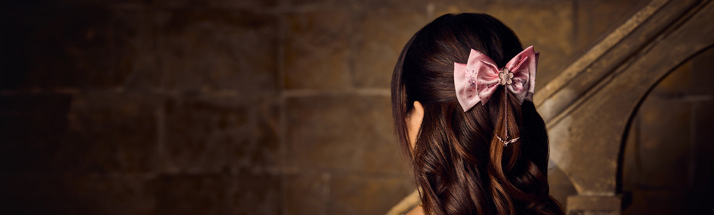 Person with a pink sakura bow in their hair standing against a stone wall.