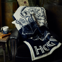 Navy and white blanket with 'Hogwarts' design draped over a chair, next to a mug on a small table.