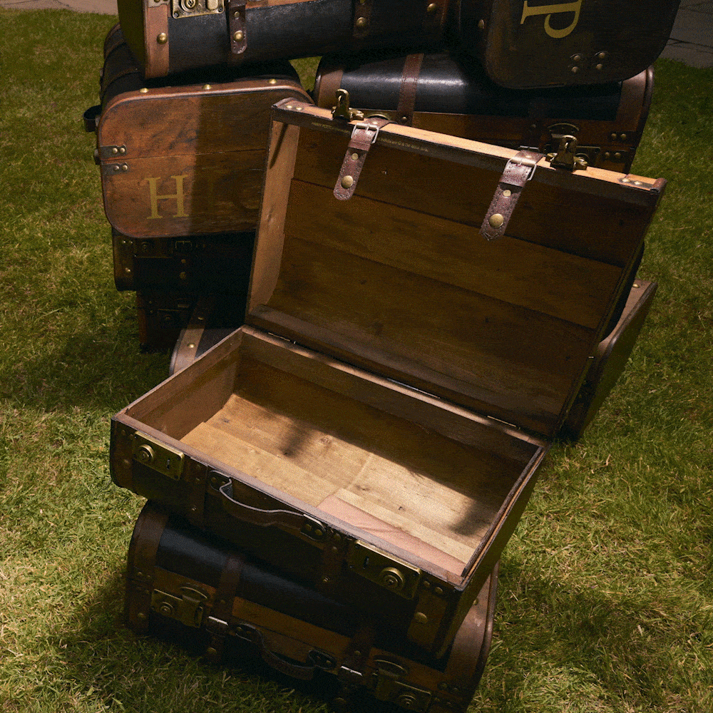 GIF featuring an open Harry Potter trunk on grass, filled with products in, including Chocolate Frog, Gryffindor Scarf, Gryffindor house robe, wand, Acceptance Letter, Time Turner necklace, small Hedwig soft toy