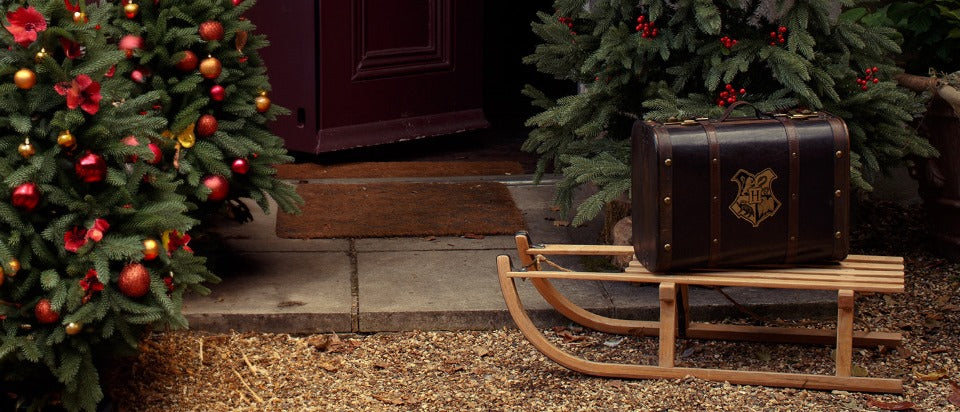 Decorative Christmas scene with a Hogwarts Trunk and sleigh in front of a door.