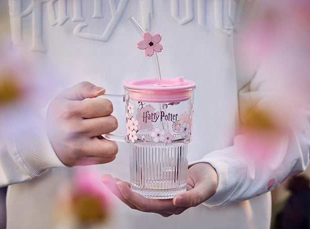 Person holding a Harry Potter-themed tumbler with a pink lid and cherry blossom design.