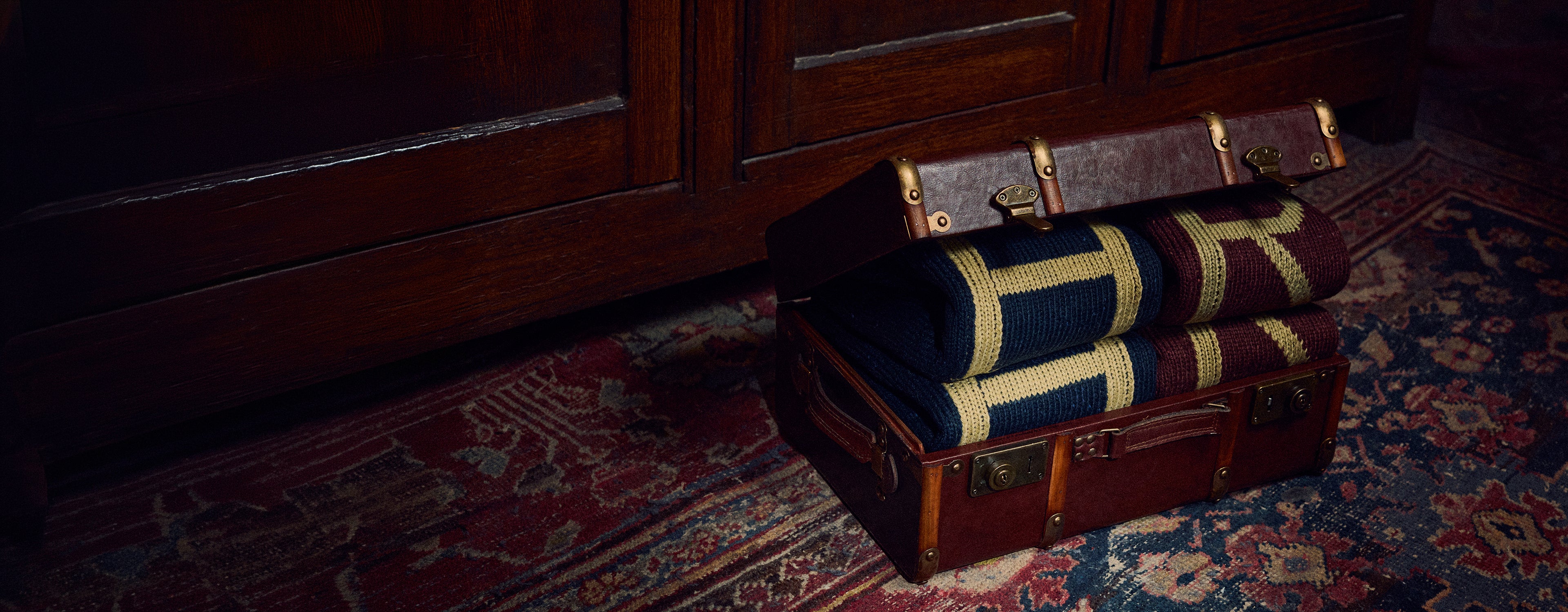 Vintage suitcase with rolled-up H and R Sweaters on a patterned rug
