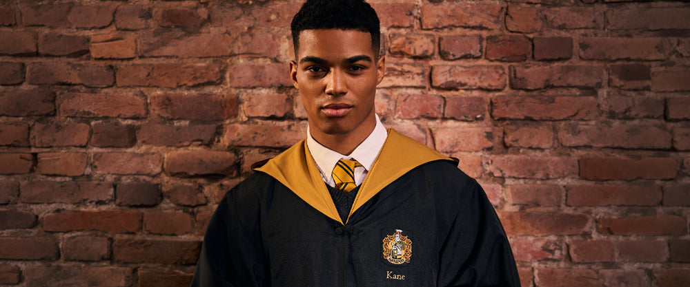 Person wearing a Hufflepuff robe with gold accents and a school emblem against a brick wall.