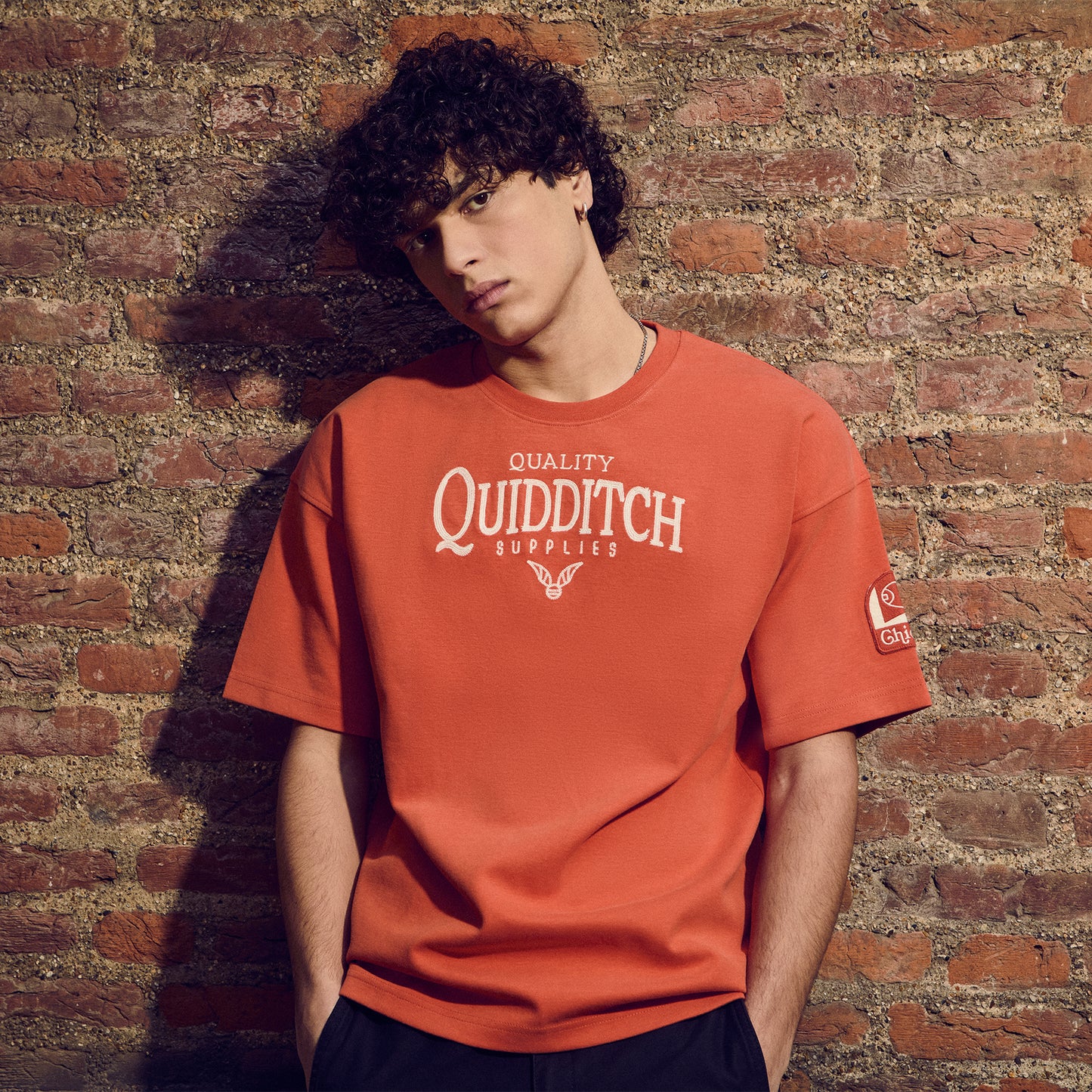 Person wearing a red Chicago 'Quality Quidditch Supplies' t-shirt against a brick wall.