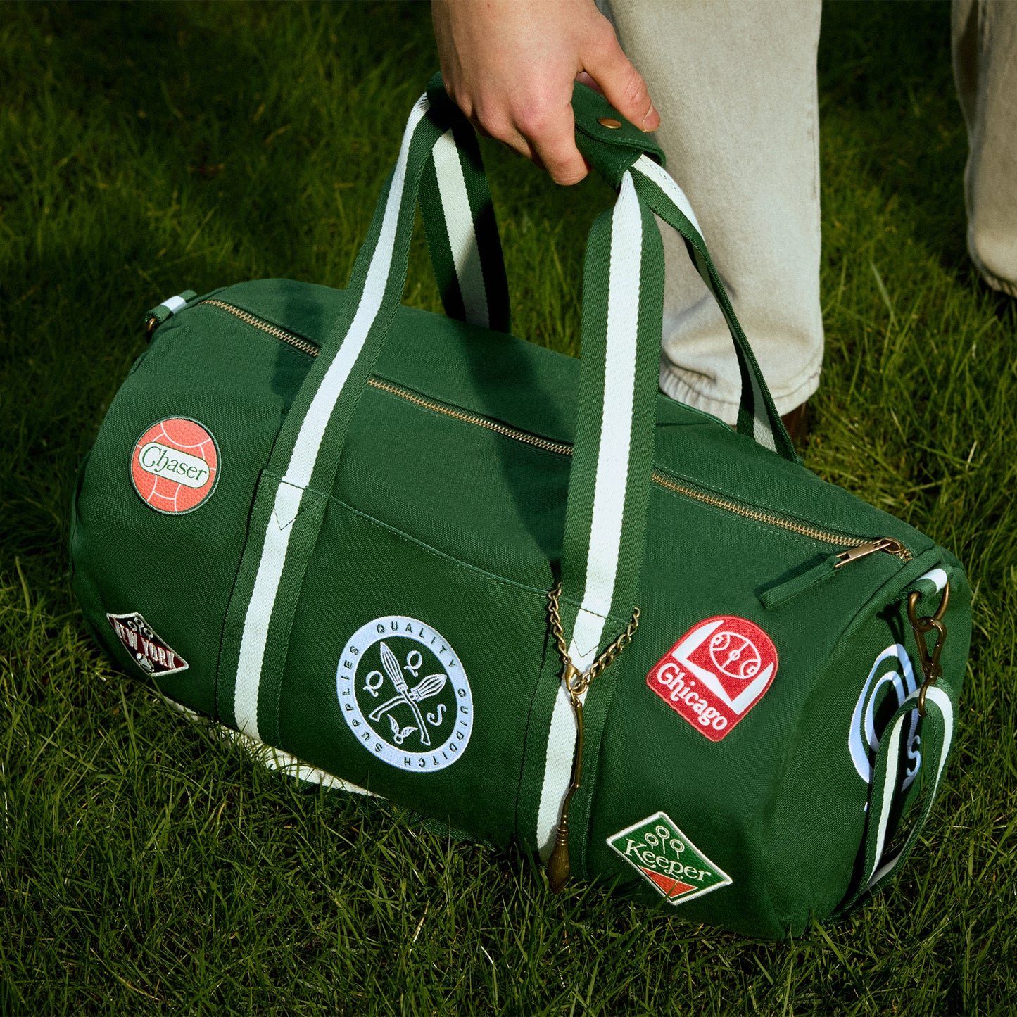 Green duffel bag with various Quidditch patches held by a person on grass