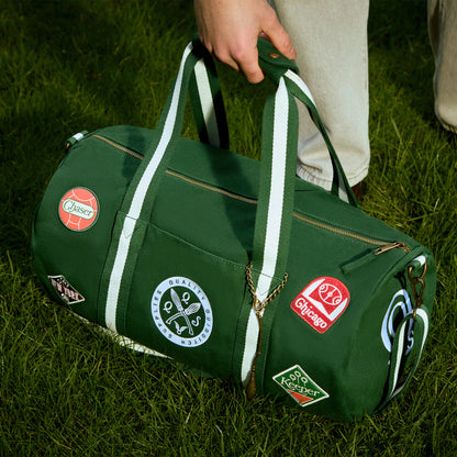 Green duffel bag with various Quidditch patches held by a person on grass