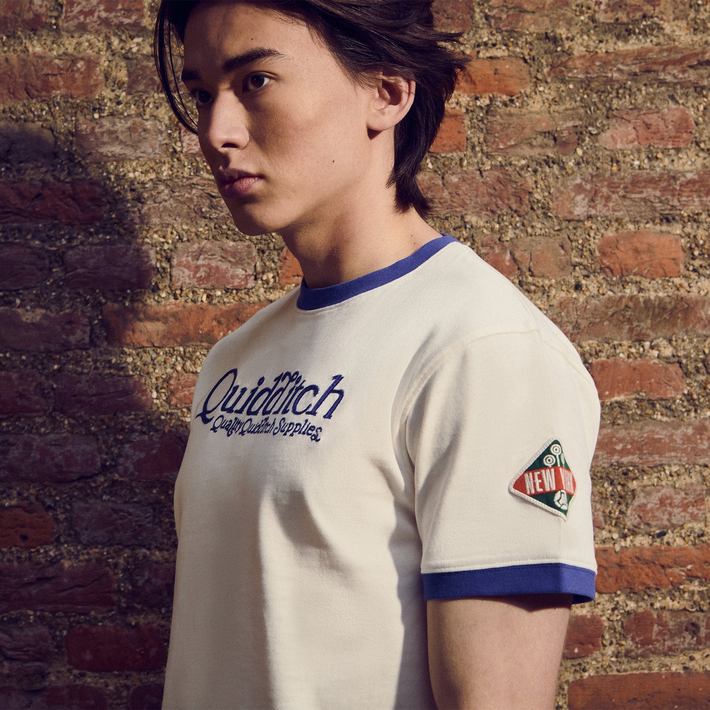 Person wearing a 'Quidditch' themed t-shirt against a brick wall