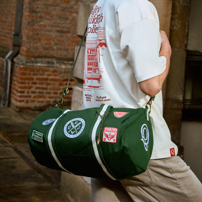 Person holding a green Quidditch duffel bag with various patches against a brick wall background