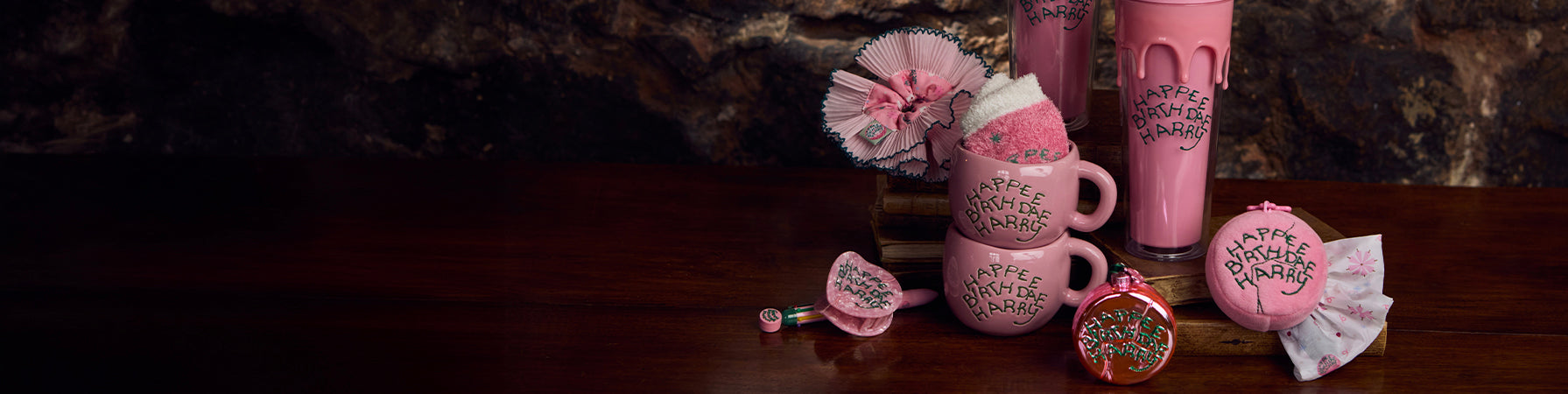 Pink ceramic mugs and decorative items on a dark surface with a stone wall background