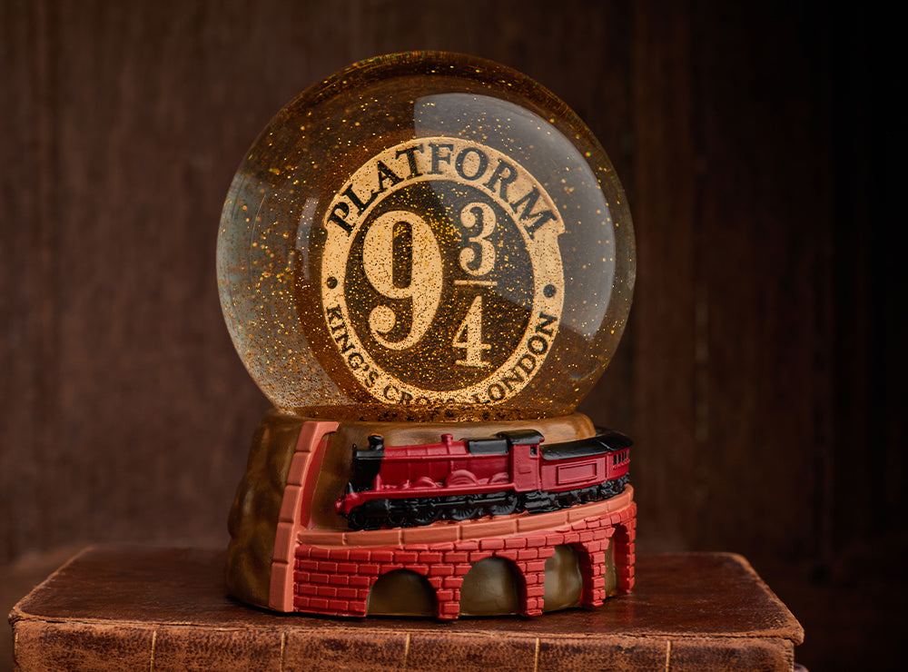 A Platform 9/4 sign inside a snow globe, surrounded by gold glitter and the Hogwarts Express at the base.