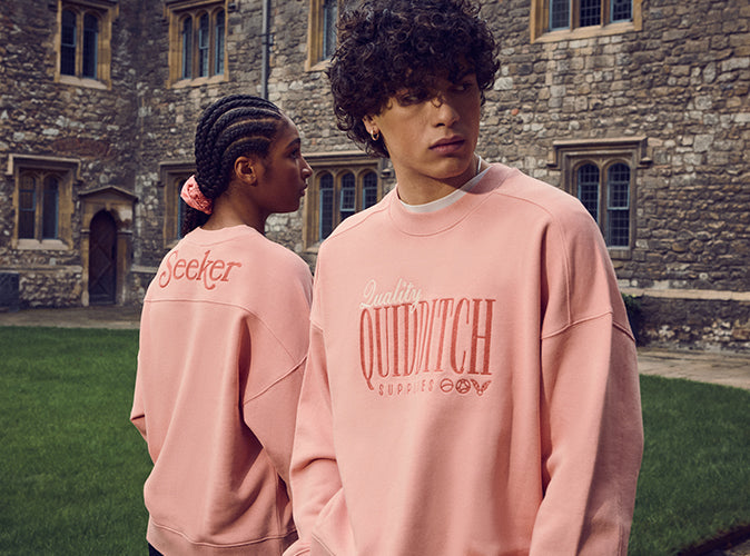 Two people wearing pink 'Quidditch' sweatshirts in front of a stone building.