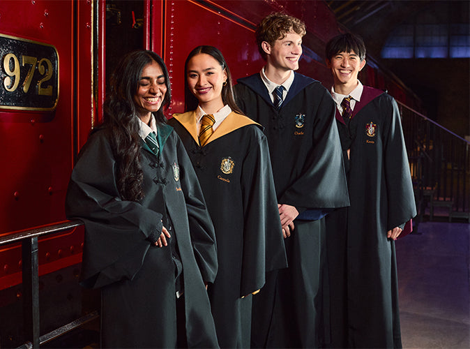 Four young people wearing Hogwarts house robes and ties stand together in front of a red train car, with the number 972 visible on the side.
